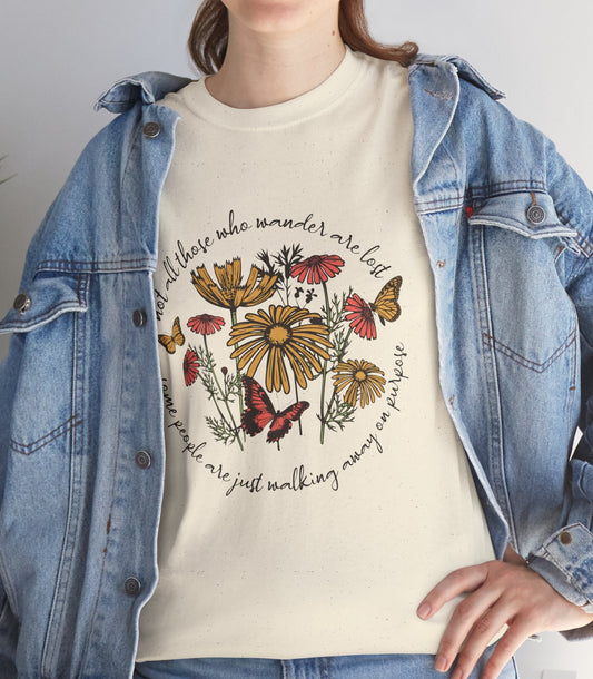 A person wearing a cream graphic T-shirt under an open light-wash denim jacket, paired with blue jeans. The T-shirt features a colorful floral and butterfly print with cursive text.