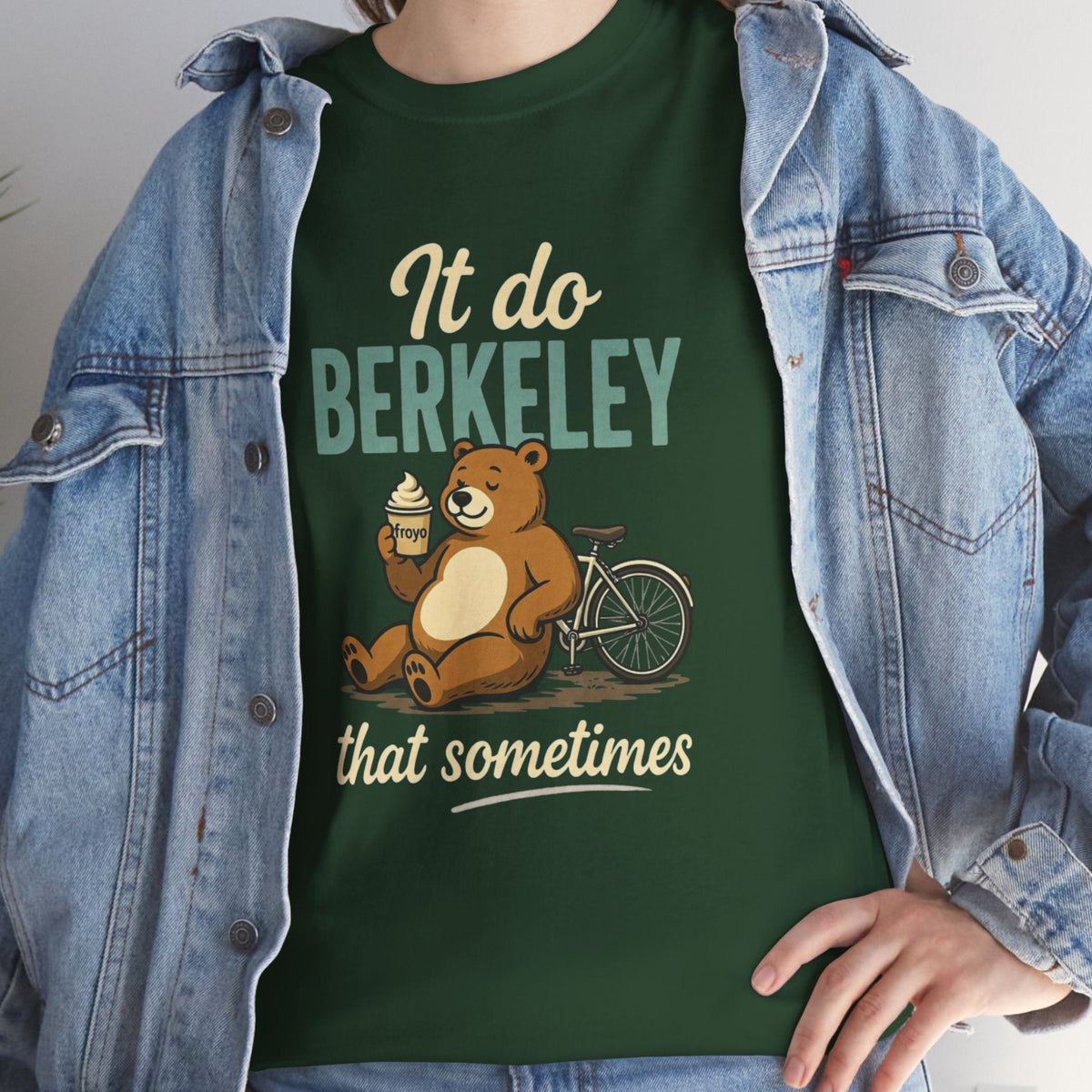 A person wearing a dark green graphic t-shirt with a cartoon bear and the text 'It do BERKELEY that sometimes', styled with an open light-wash denim jacket.
