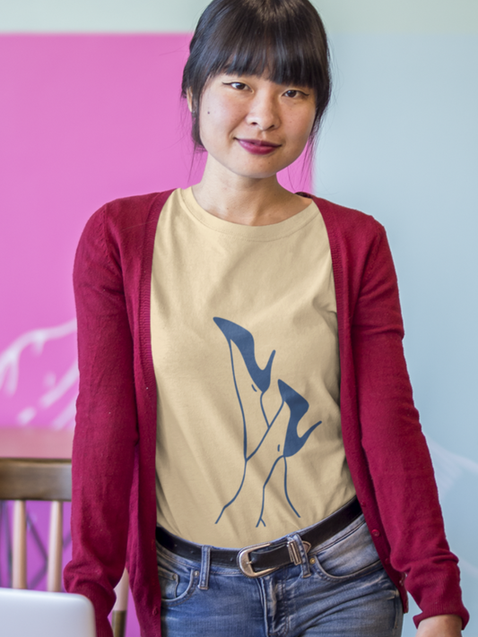 A woman with dark hair and bangs stands behind a wooden desk in an office setting. She is wearing a beige graphic t-shirt under a maroon cardigan, paired with blue jeans.