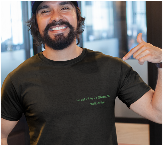 A smiling man wearing a dark charcoal gray t-shirt with green text on the chest that reads 'C. del H / a / r's 'stempli', 'hello tribe'.