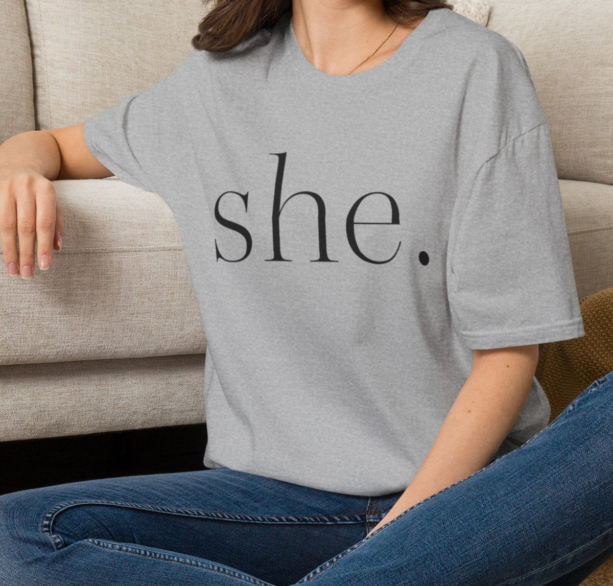 Person sitting on a carpeted floor wearing a gray t-shirt with text and graphics, in a home setting.