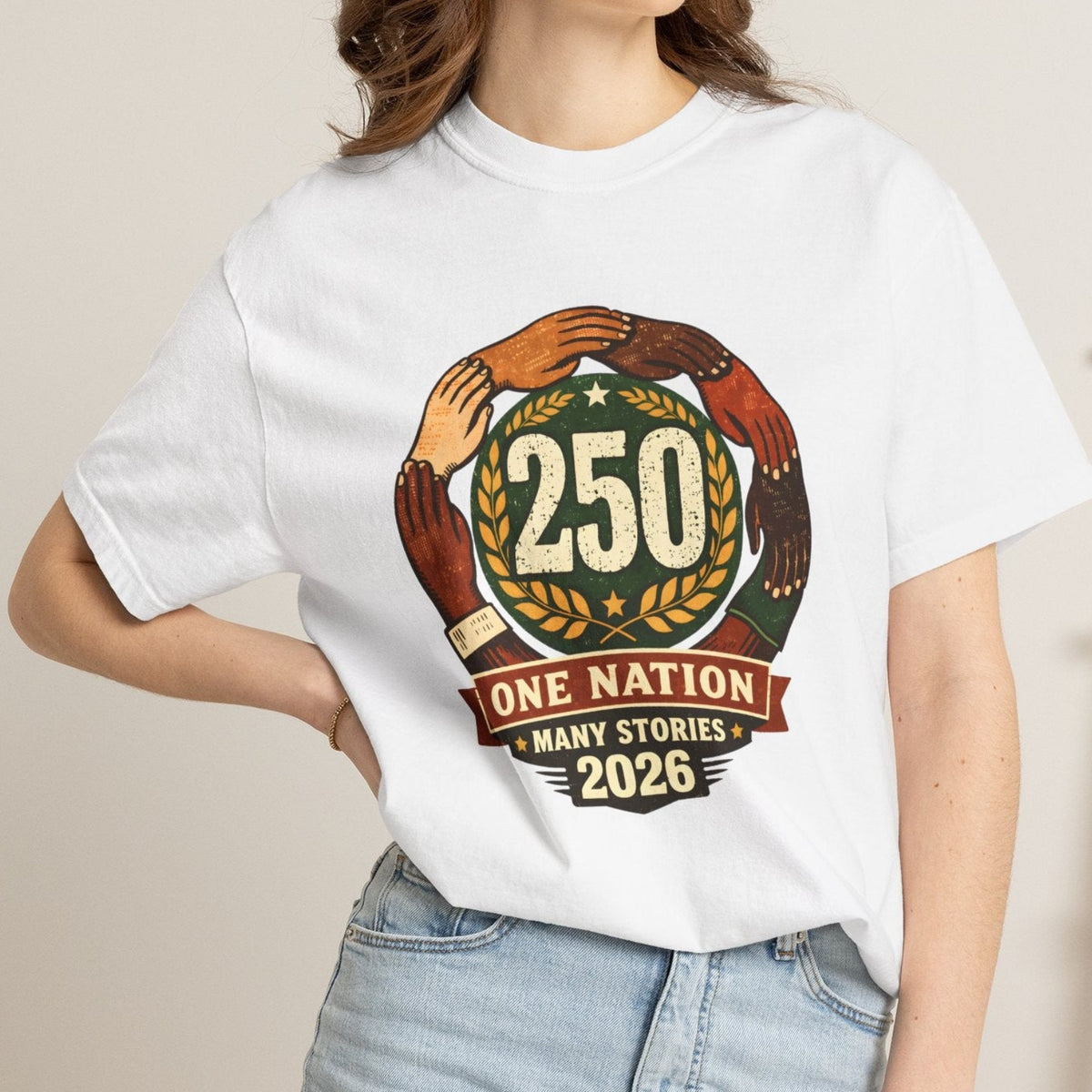 A woman wearing a white graphic t-shirt with a '250 One Nation Many Stories 2026' design, paired with light blue denim shorts, standing in a brightly lit room.
